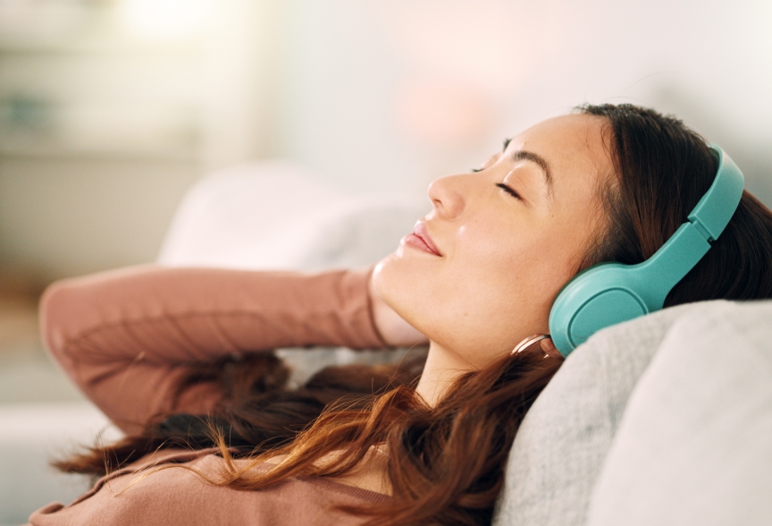 A woman relaxing on a sofa with headphones on, eyes closed