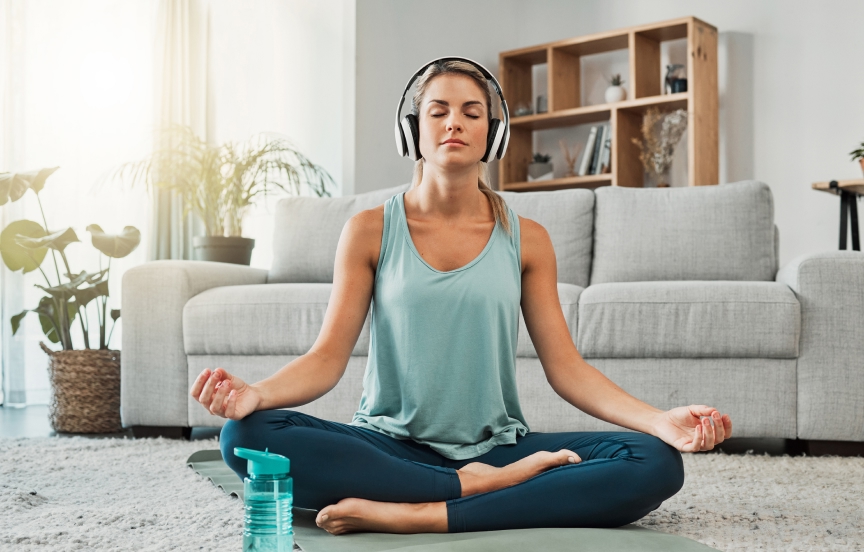 A woman meditating in a calm living room with headphones on